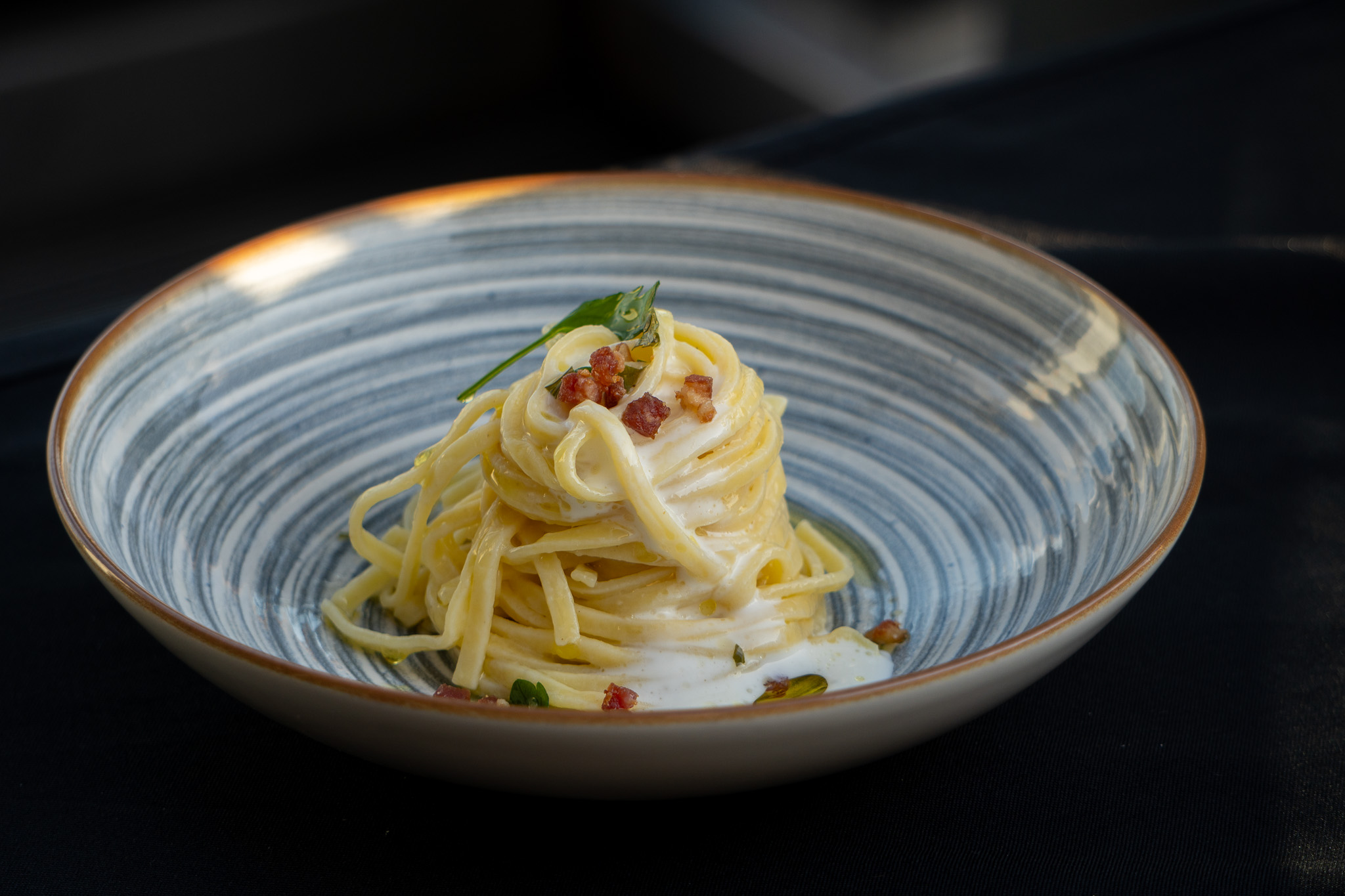 Nahaufnahme von einem Teller mit al dente Spaghetti in cremiger Sauce, garniert mit knusprigen Speckwürfeln und einem Basilikumblatt, appetitliches Catering-Gericht