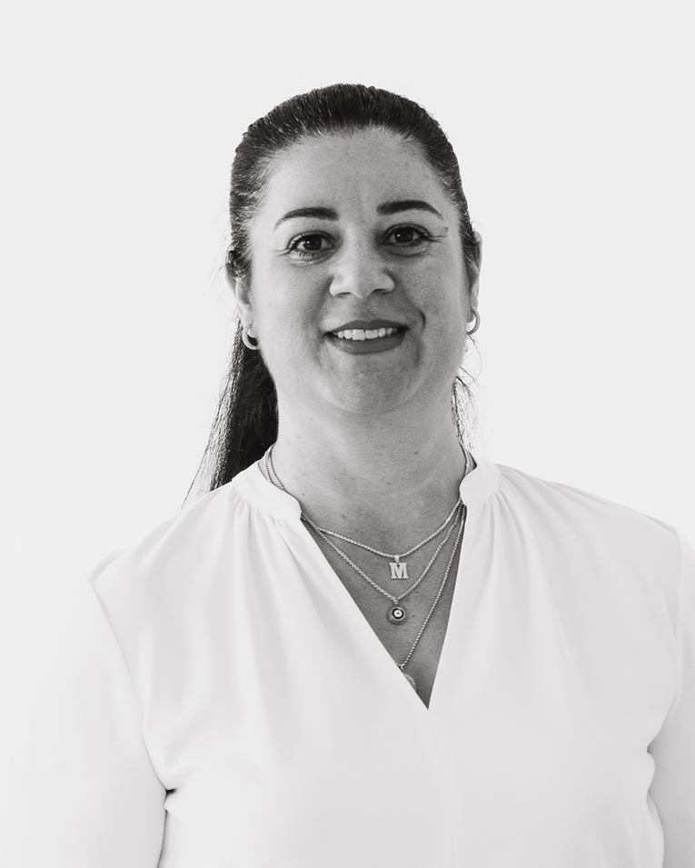 Schwarz-weiß Porträt einer lächelnden Frau mit zurückgebundenen dunklen Haaren und hellem Oberteil, die Halsketten trägt, Teammitglied des Catering-Unternehmens