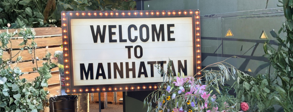 Beleuchtetes Willkommensschild „Welcome to Mainhattan" bei einem Corporate Event Frankfurt, umrahmt von Blumen und Grünpflanzen.