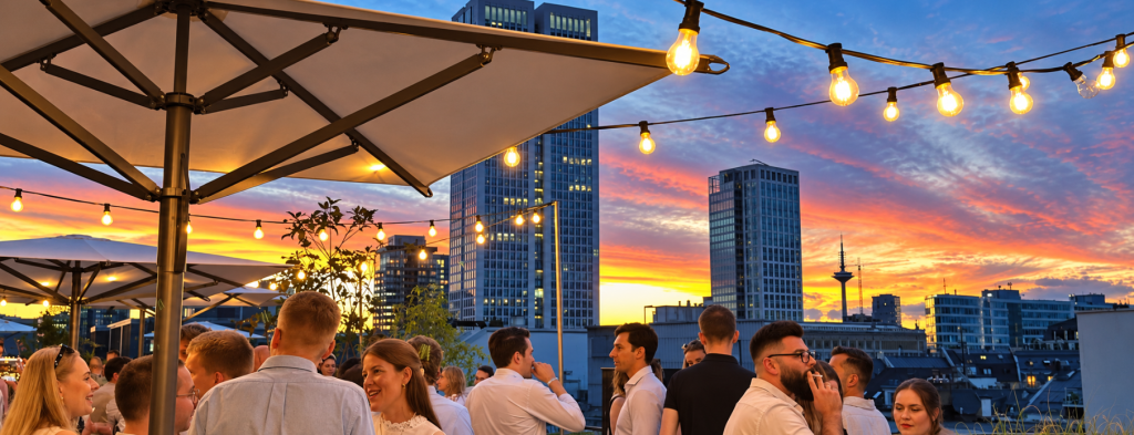 Rooftop-Party beim Sonnenuntergang mit Lichterketten und Skyline – Corporate Event Frankfurt mit stilvollem Ambiente.