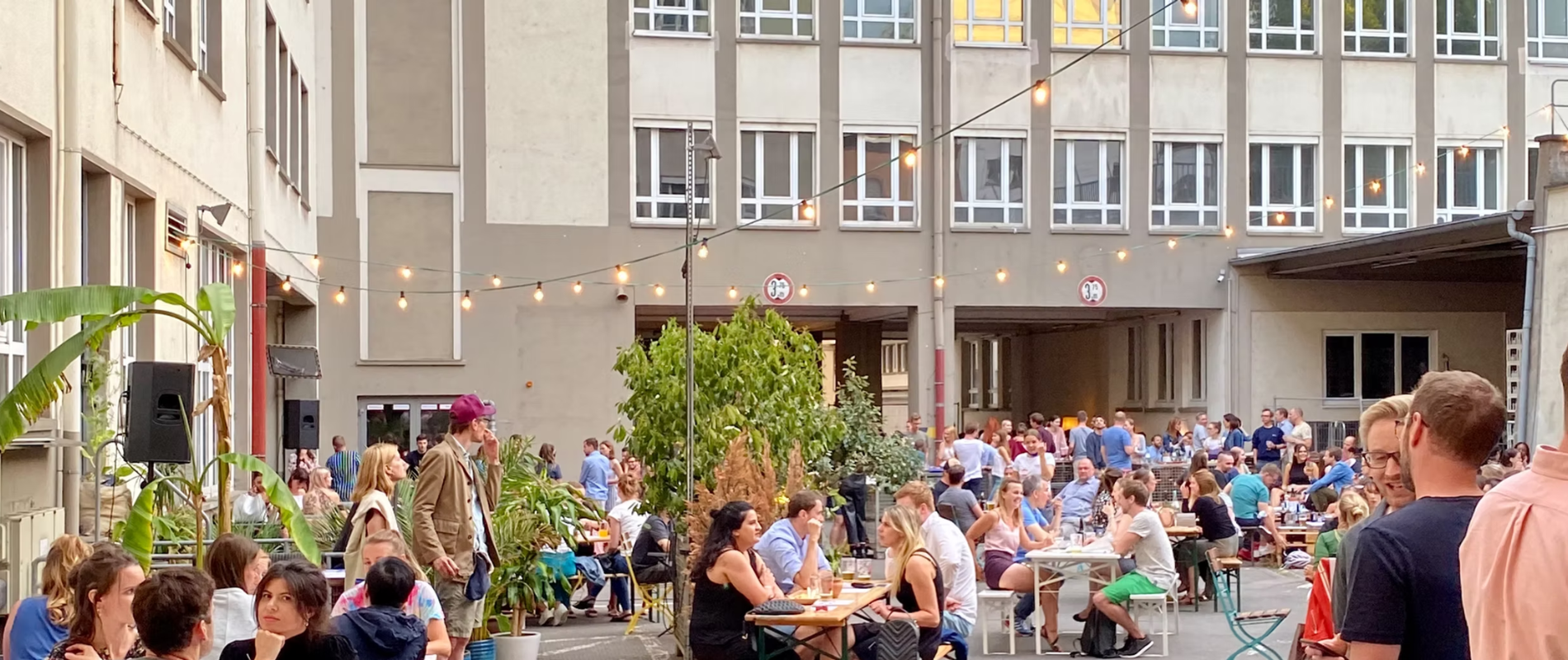 Sommerliches Corporate Event Frankfurt mit vielen Gästen an Tischen in einem belebten Innenhof mit Lichterketten.