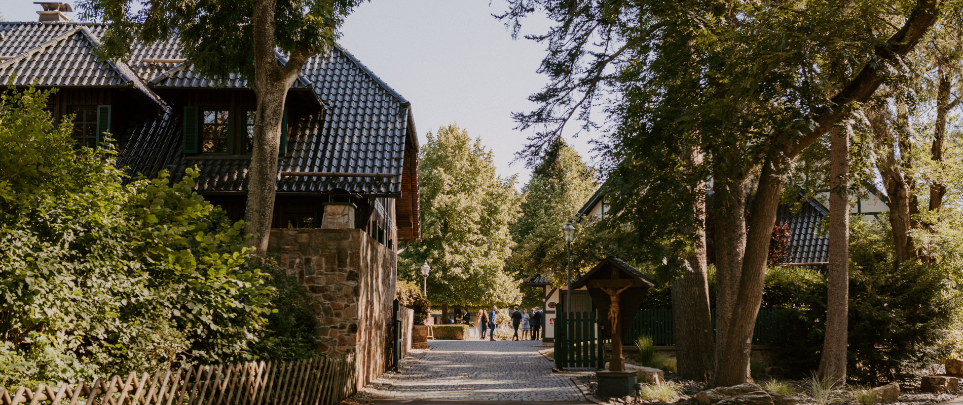 Gepflasterter Weg eines Corporate Event Frankfurt Geländes mit historischen Fachwerkhäusern, Bäumen und einem Wegkreuz.