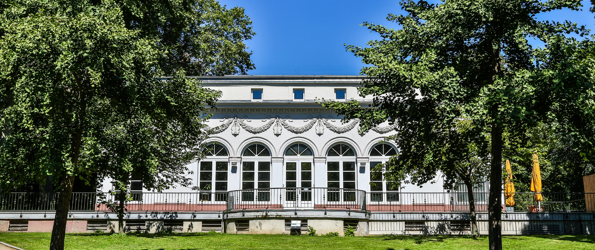 Klassische Veranstaltungslocation in Frankfurt mit weißer Fassade und Arkadenfenstern, ideal für Corporate Events Frankfurt, umgeben von Grünanlage.