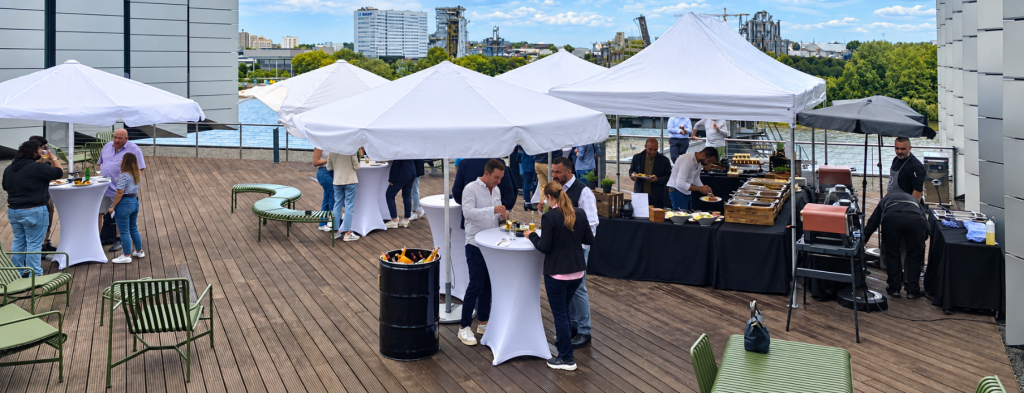 Outdoor-Empfang mit Catering Frankfurt auf einer Dachterrasse am Wasser mit weißen Zelten und Gästen.