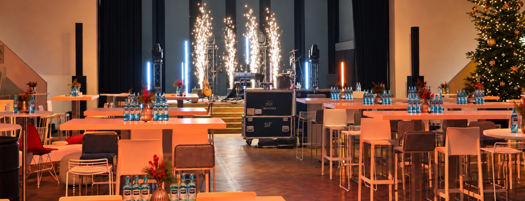 Festlich dekorierte Eventhalle mit Stehtischen, Bühne und Pyrotechnik – Corporate Event Frankfurt mit Catering-Setup und Weihnachtsbaum.