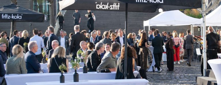 Elegantes Corporate Event Frankfurt mit Gästen unter fritz-kola Sonnenschirmen auf einem Außengelände mit Stehtischen.